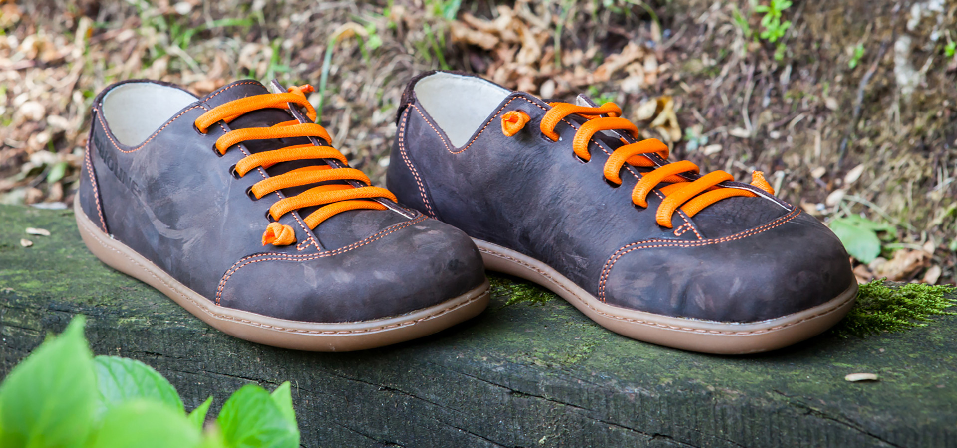 Scarpe marroni con lacci arancioni appoggiate su una panca all’aperto.