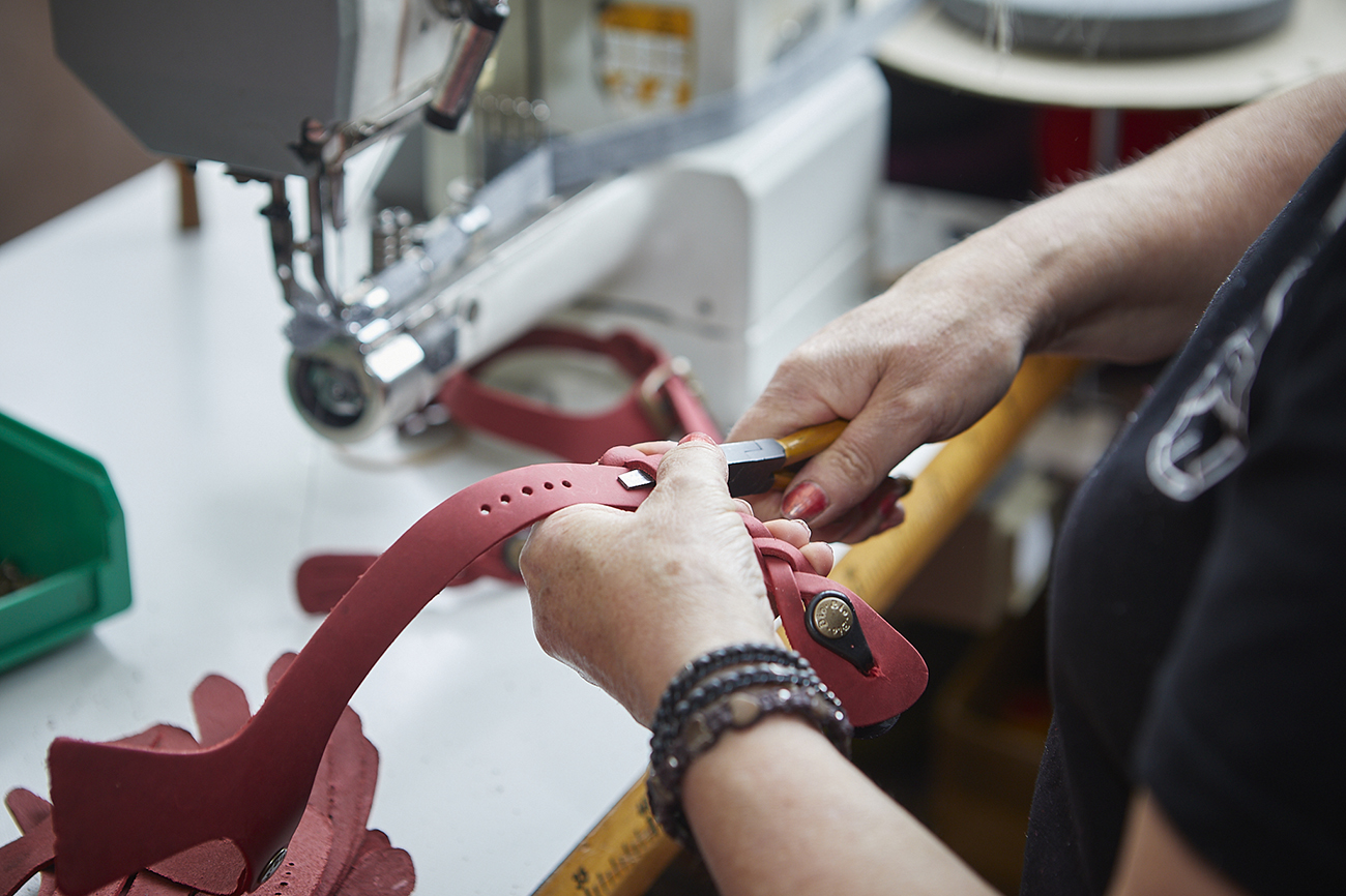 Pressatura di cinturini intrecciati in pelle rossa su macchina da lavoro.