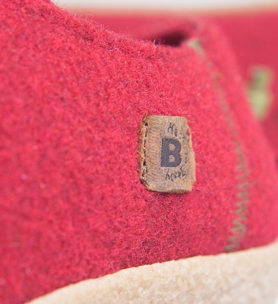 Macro su etichetta in pelle con logo B cucita su feltro rosso.