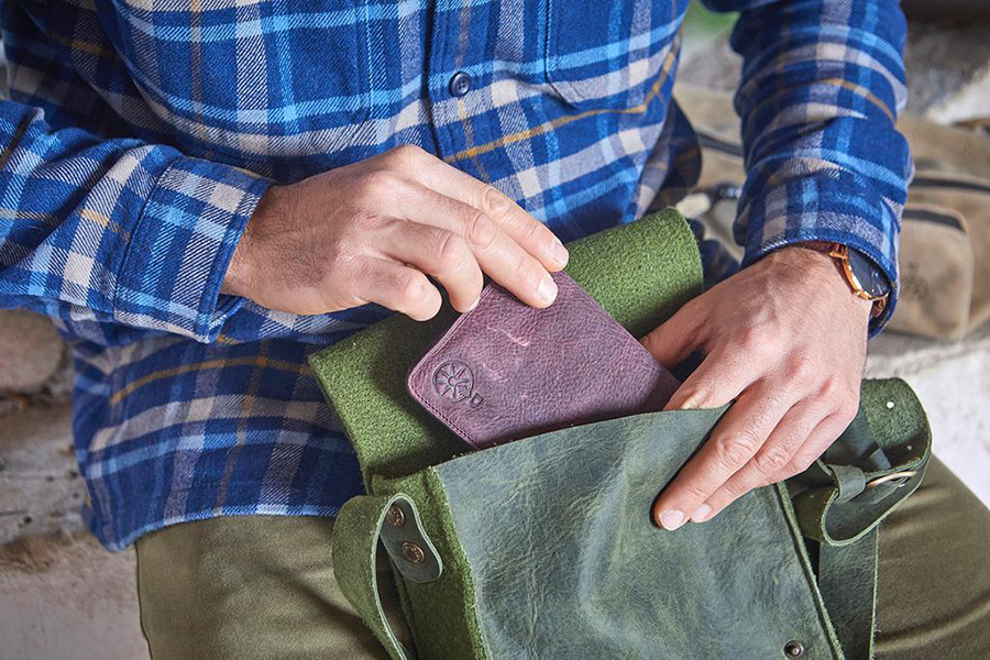 Uomo in camicia a quadri inserisce un portafoglio in una borsa verde