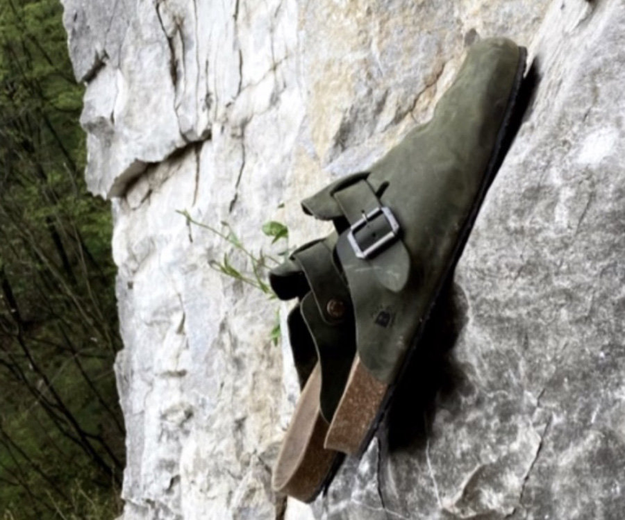 Sandalo verde militare Bioline appoggiato su parete rocciosa in ambiente naturale.