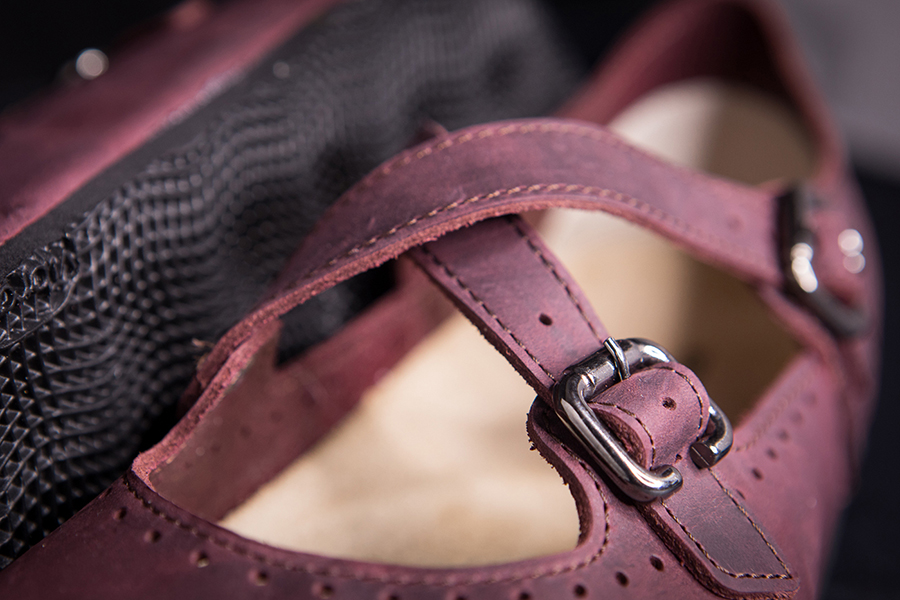Dettaglio fibbia su scarpa in pelle bordeaux con suola nera antiscivolo.