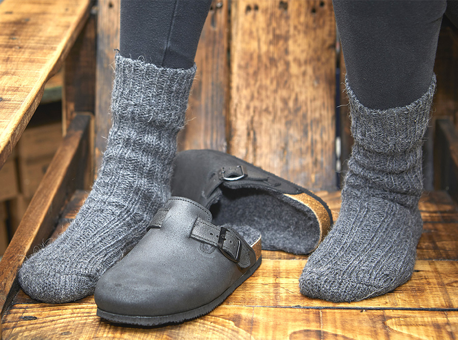 Scarpe nere Bioline con calzini grigi su pavimento in legno.