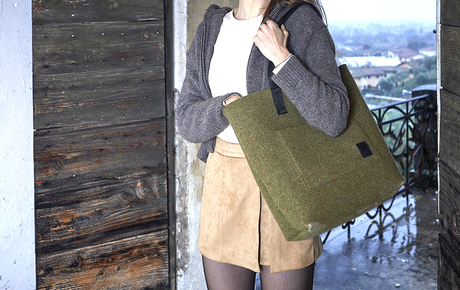 Donna con borsa verde in feltro davanti a porta in legno.