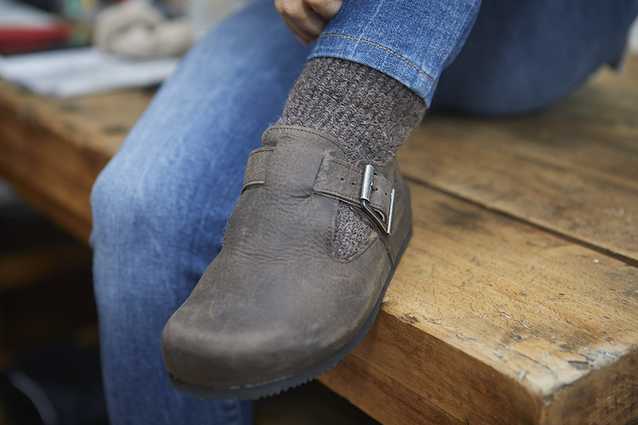 Scarpa marrone con calza grigia su jeans e tavolo in legno
