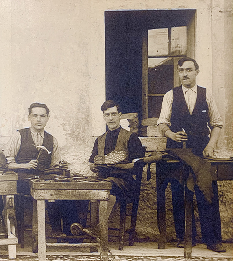 Tre calzolai posano davanti alla bottega con attrezzi del mestiere.