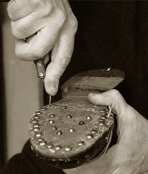 Mani che cuciono una suola con borchie su scarpa tradizionale.