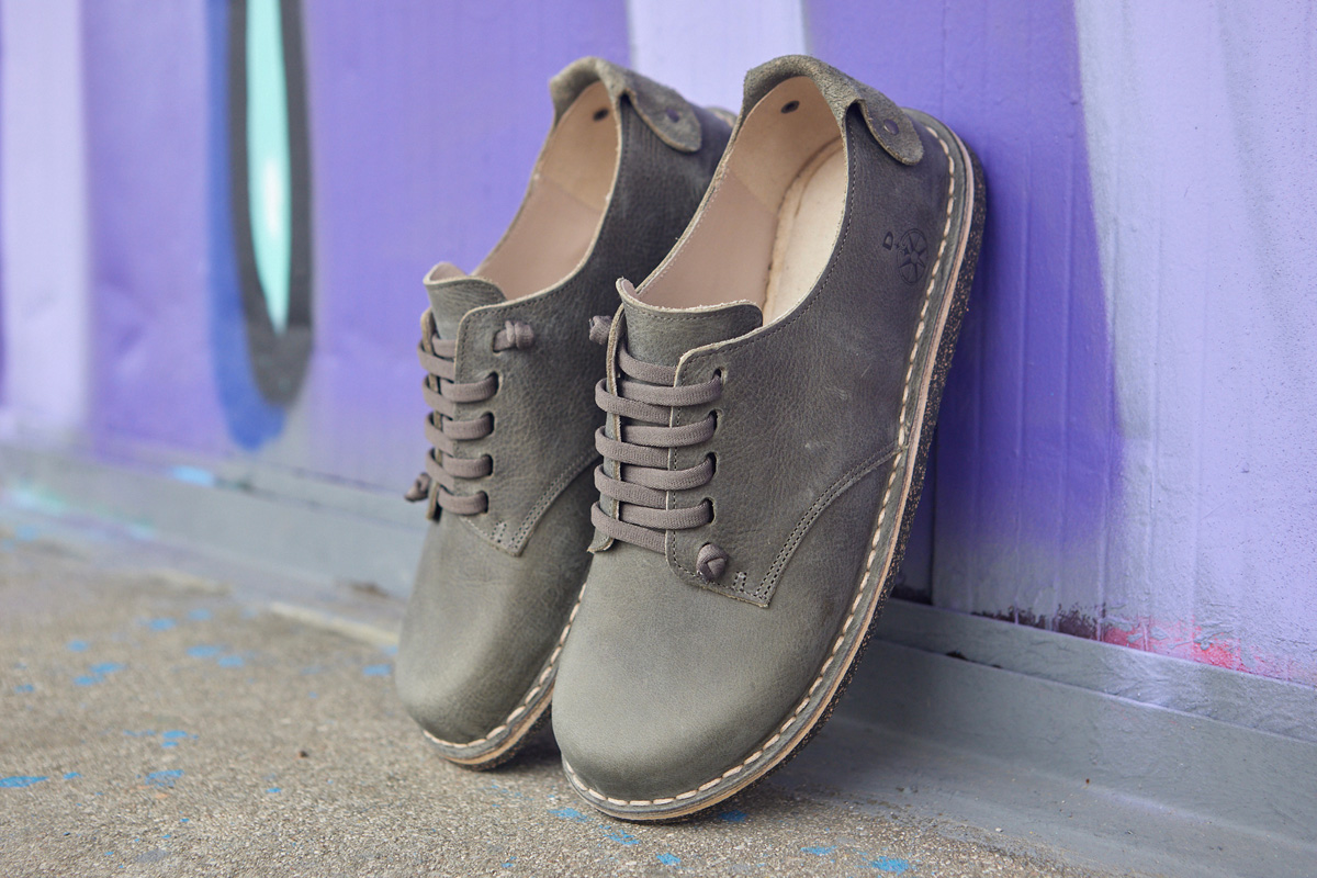 Scarpe stringate Bioline grigie appoggiate a parete lilla.