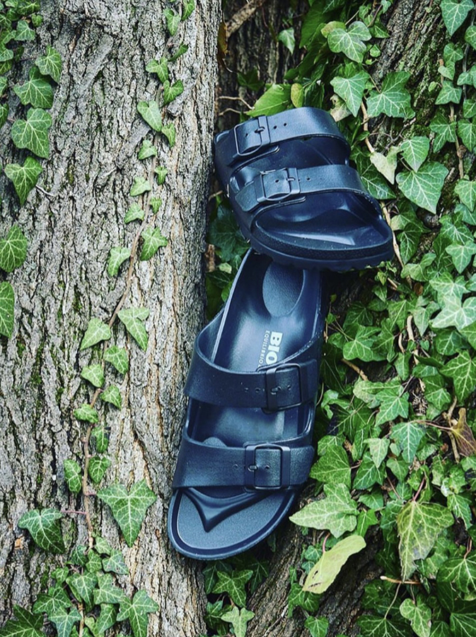 Sandali neri Bioline in plastica appoggiati su tronco con edera.
