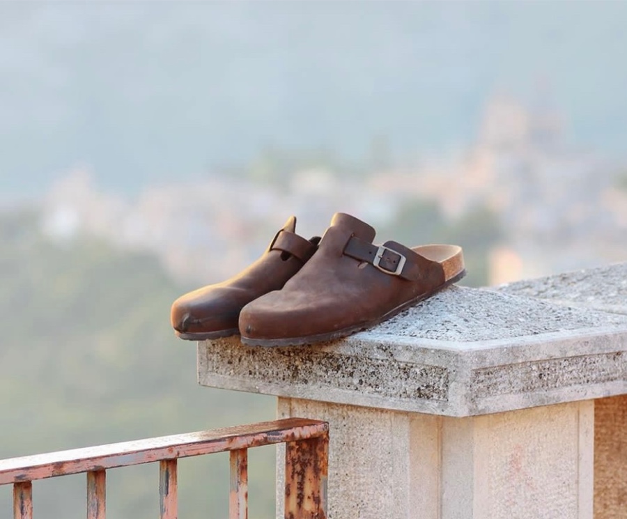 Clogs marroni Bioline su muretto con vista panoramica.