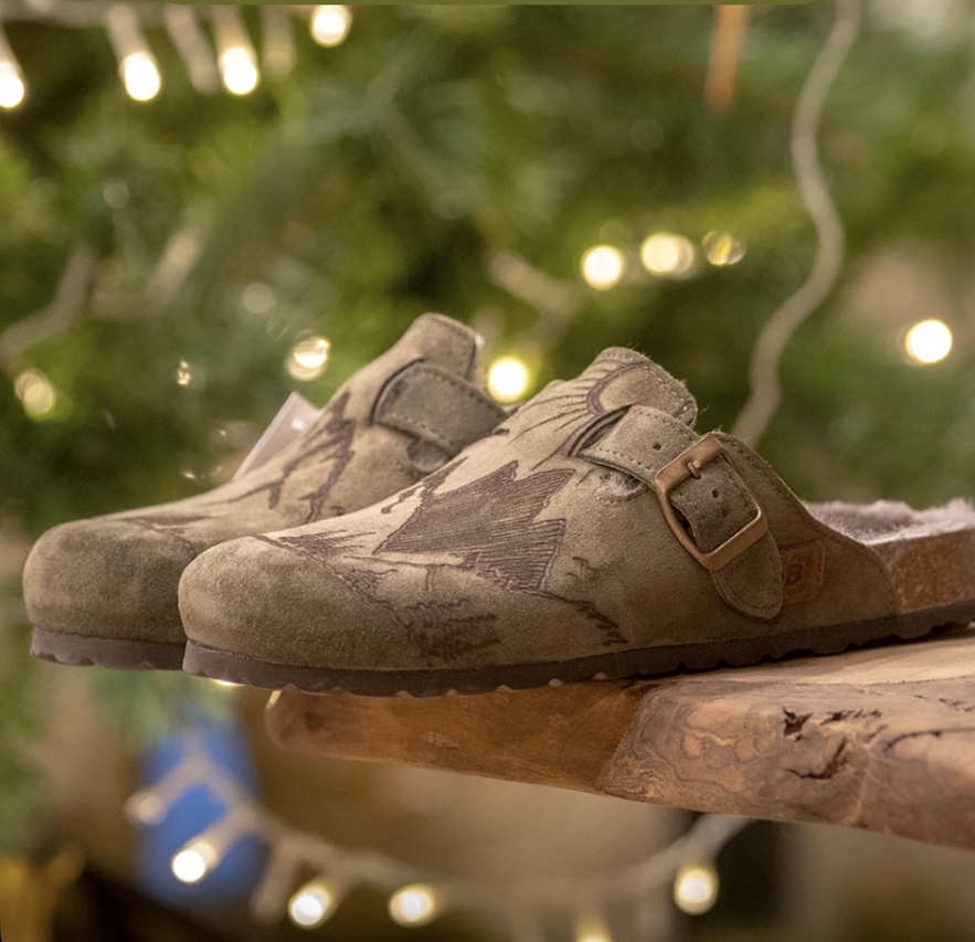 Clogs verdi Bioline con fibbia su sfondo natalizio.