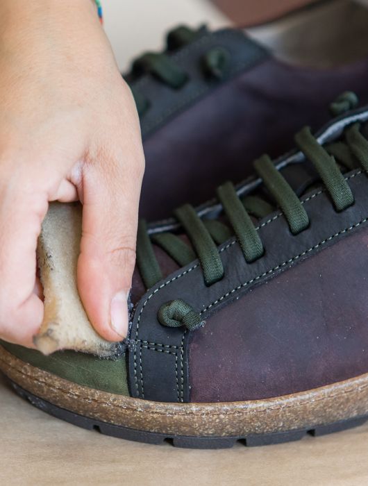 Mano che pulisce o rifinisce una scarpa con lacci verdi e suola in sughero.