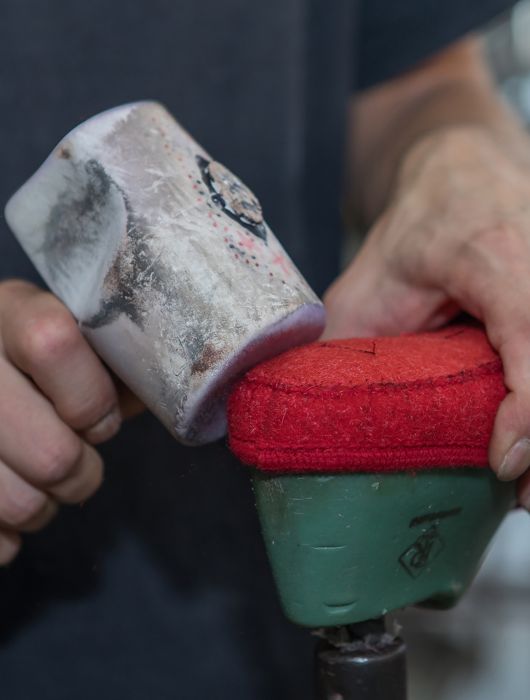 Delle mani pressano tomaia rossa su forma con un martello da calzolaio durante la lavorazione.