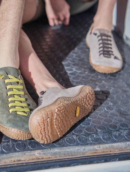 Close-up of several people sitting on a metal surface, wearing minimalist shoes in different colours; a flexible rubber sole is clearly visible in the foreground.