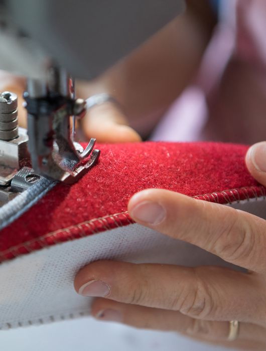 Delle Mani cuciono una tomaia rossa con macchina da cucire industriale durante la produzione.