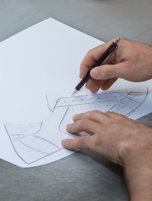 Hands drawing a technical model for a shoe on paper with a mechanical pencil.