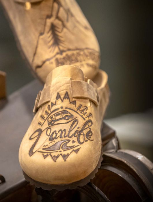 Un sabot Bioline in legno con una scritta e un disegno di un van, montagne e onde incise.