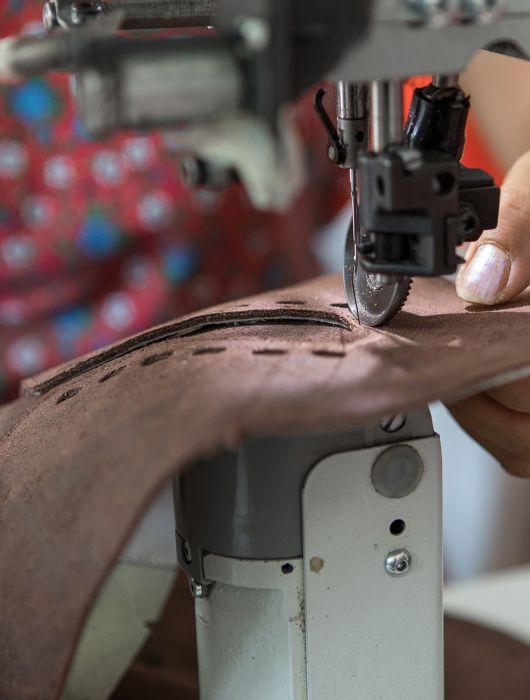 Mano che cuce una tomaia in pelle con una macchina da cucire industriale.